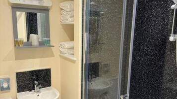 Baño con ducha acristalada, lavabo, inodoro y perchero para toallas.