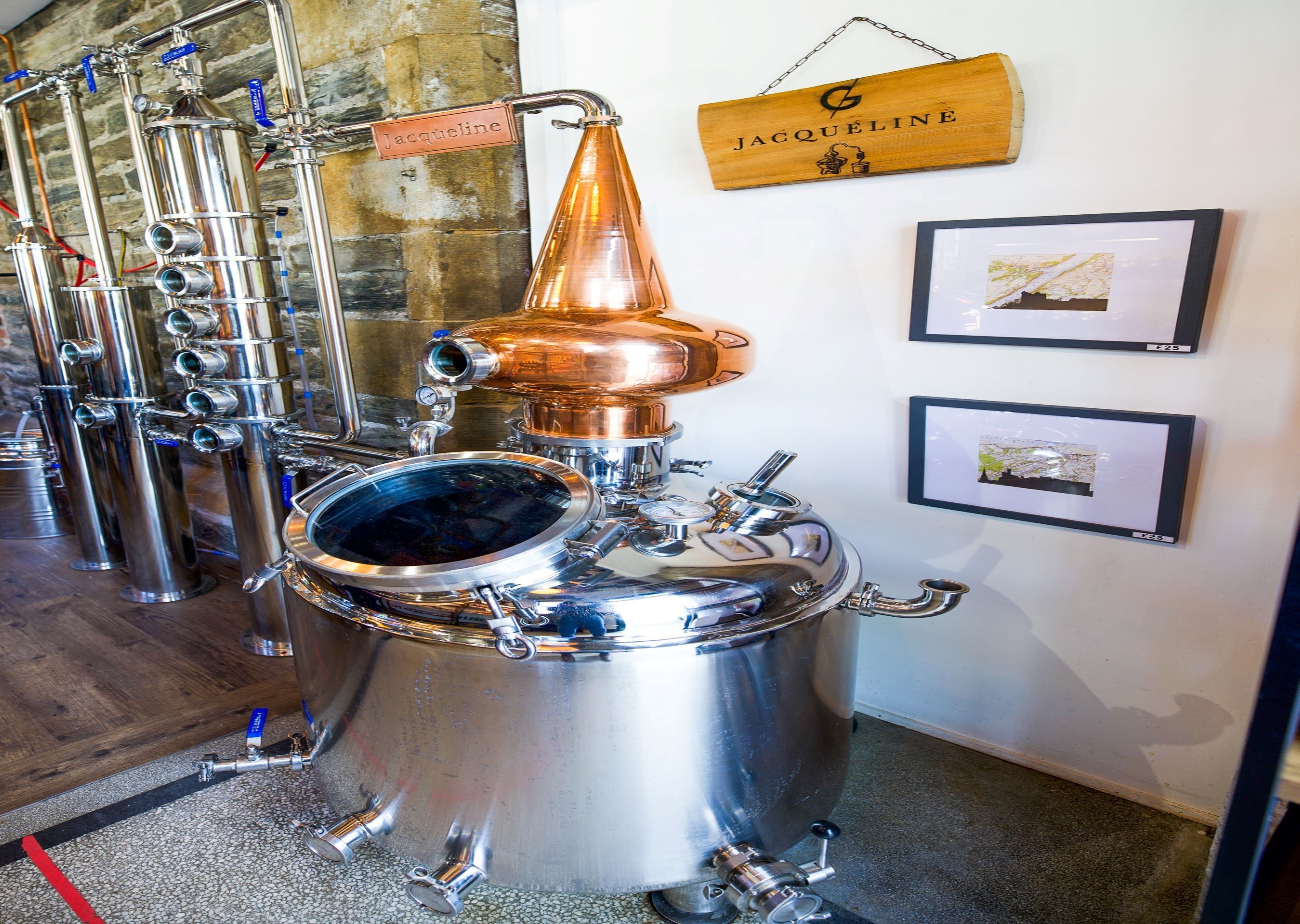 A distillery with stainless steel equipment, a copper still, and a wooden sign with the name 'Jacqueline'.