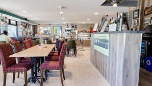 A restaurant with a long wooden table, plaid chairs, and a bar area with a wooden counter.