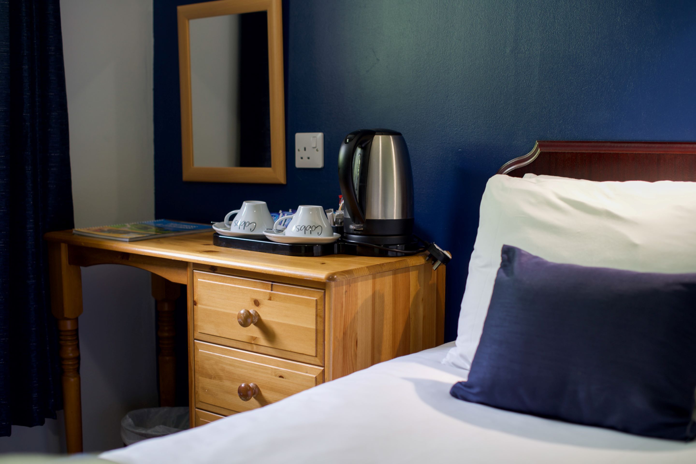 Una habitación de hotel con una cama, un escritorio de madera, una cafetera y una bandeja con tazas.