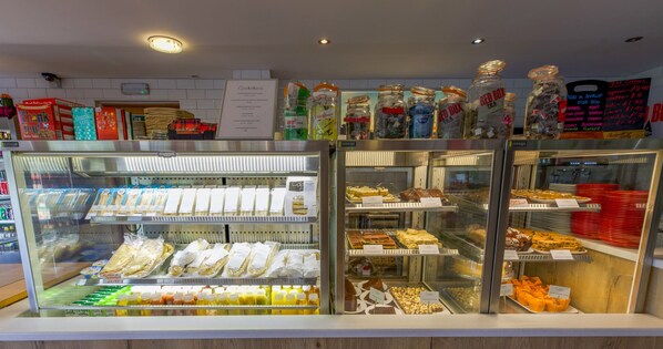 A bakery display case with various baked goods and a sign indicating the cost of adding a syrup. - Loch Ness Drumnadrochit Hotel (Inverness)