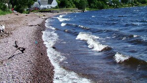 A rocky shoreline with a house and forested hills in the background.
