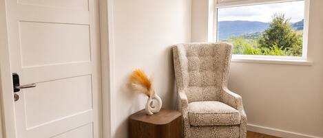 A room with a white door, a wooden side table with a vase, and a patterned armchair.