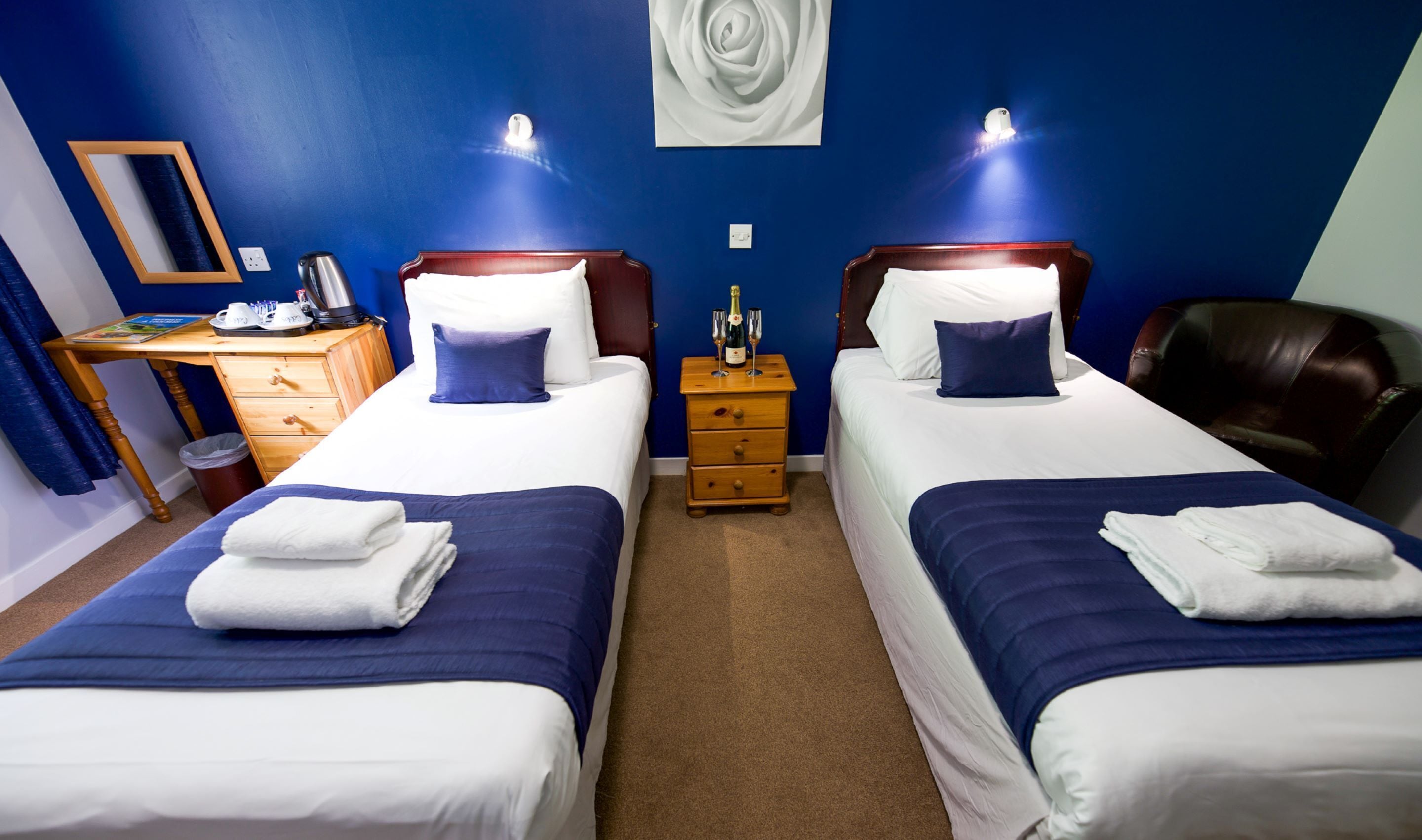 Ein Hotelzimmer mit zwei Betten, einem Holznachttisch, einem Schreibtisch und einem Stuhl.
