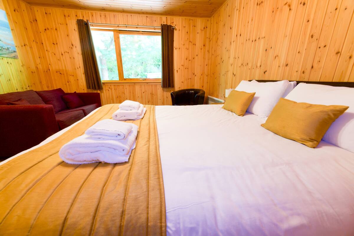 Ein Zimmer mit Holzwänden, einem Bett, einem roten Sofa und einem Fenster mit Vorhängen.