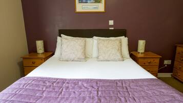 A neatly made bed with a purple blanket, two pillows, and two bedside tables with lamps.