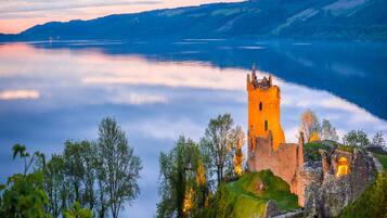 Un castillo histórico junto a un lago, con un puente que lo conecta.