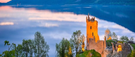 A historic castle by a lake with a bridge leading to it.