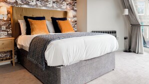 A modern hotel room with a large bed, a headboard with a textured design, and a view of the city through large windows.