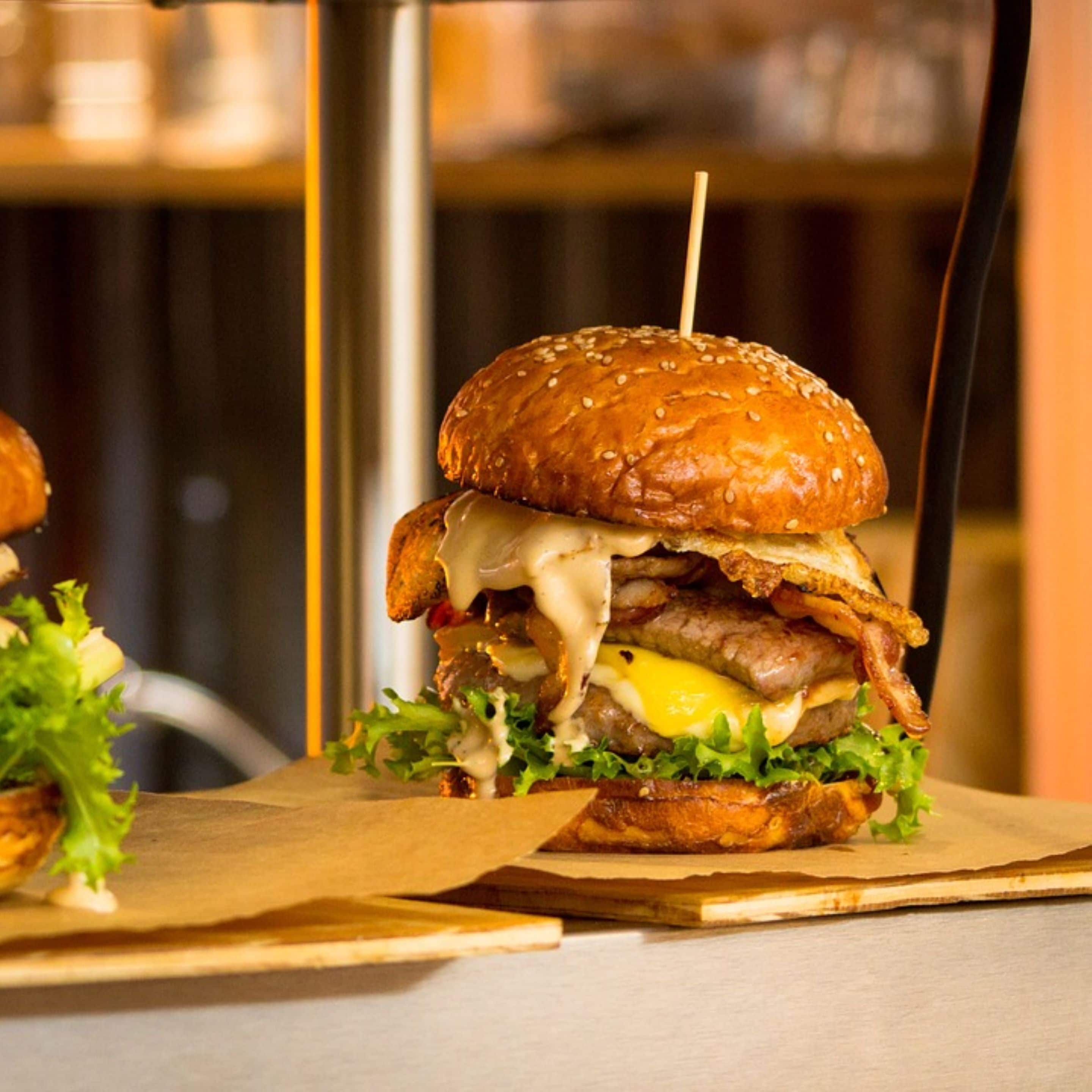 A burger with a sesame seed bun, lettuce, cheese, and a beef patty, served on a wooden board.