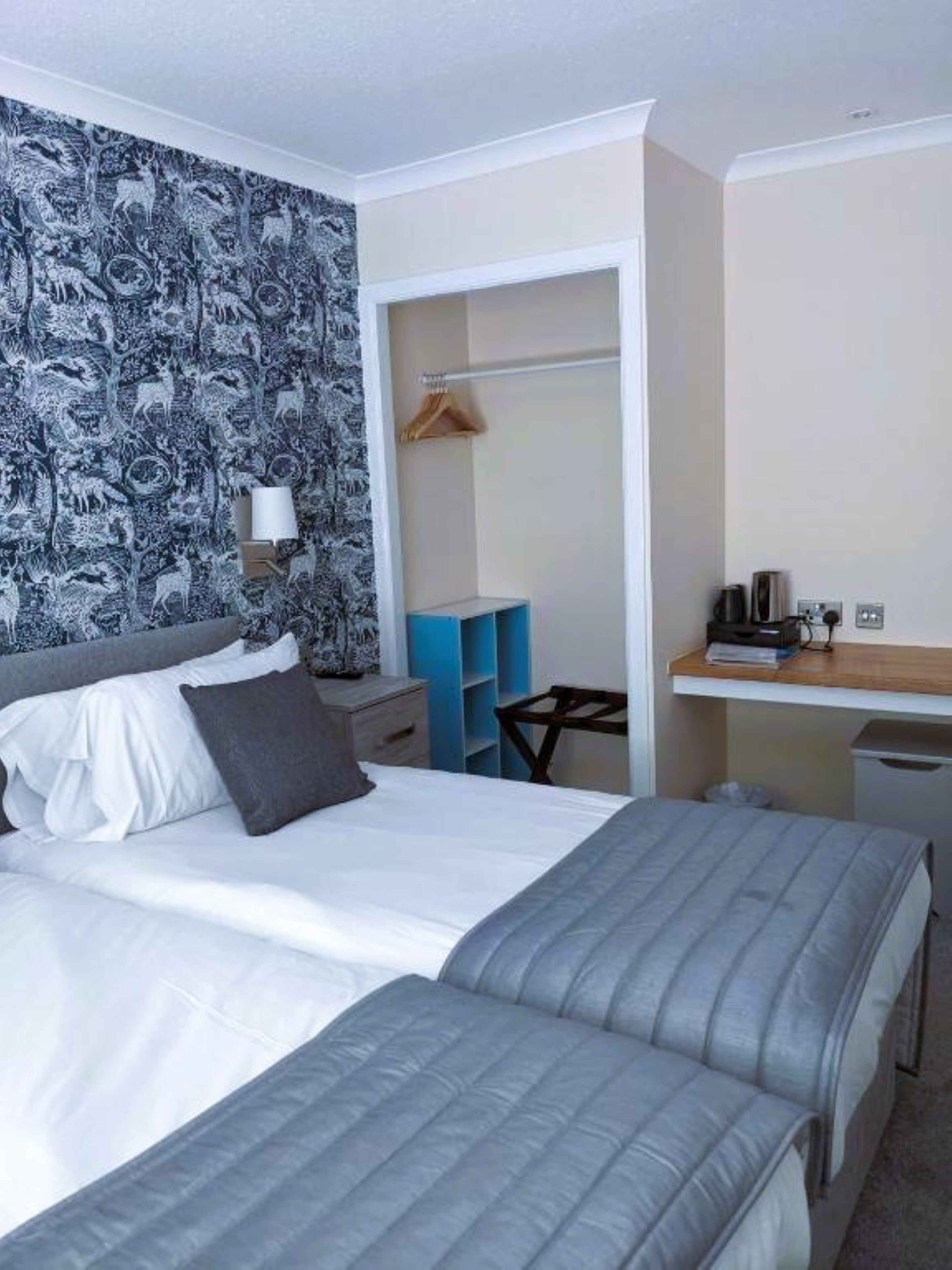 Ein Hotelzimmer mit einem großen Bett, einem kleineren Bett, einem Schreibtisch mit Stuhl, einem Kleiderschrank und einem Spiegel.