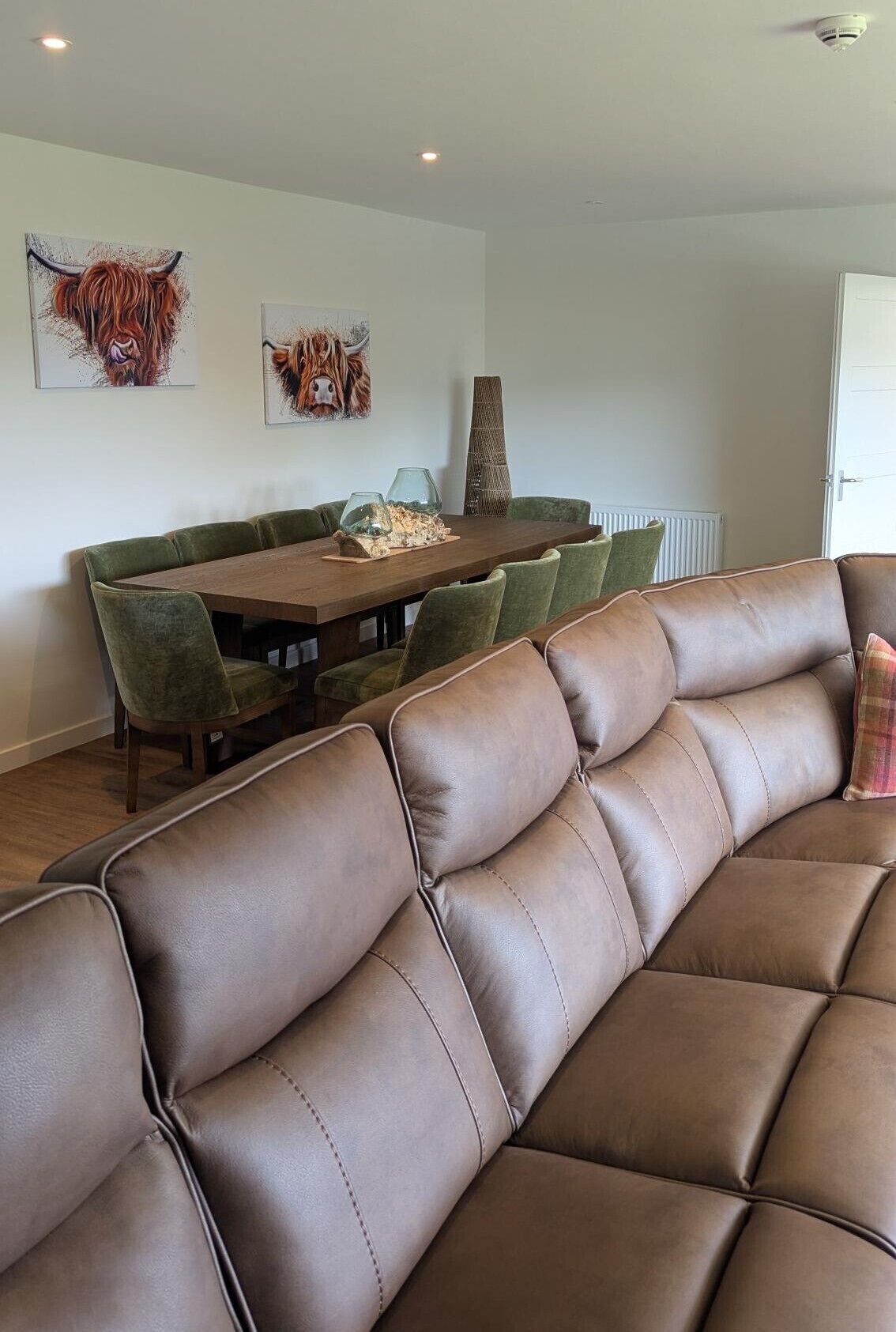 A modern living room with a brown leather sofa, a dining table with chairs, and two animal-themed wall art pieces.