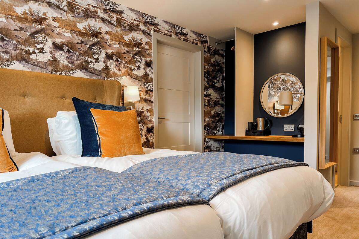 Ein Hotelzimmer mit einem großen Bett, einem Holz-Kopfteil, einer Wand mit Natur-Tapete, einem Nachttisch mit Lampe und einem Spiegel.