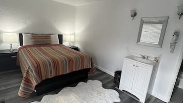 A bedroom with a bed, bedside lamps, a white rug, a vanity with a mirror, and a hairdryer.