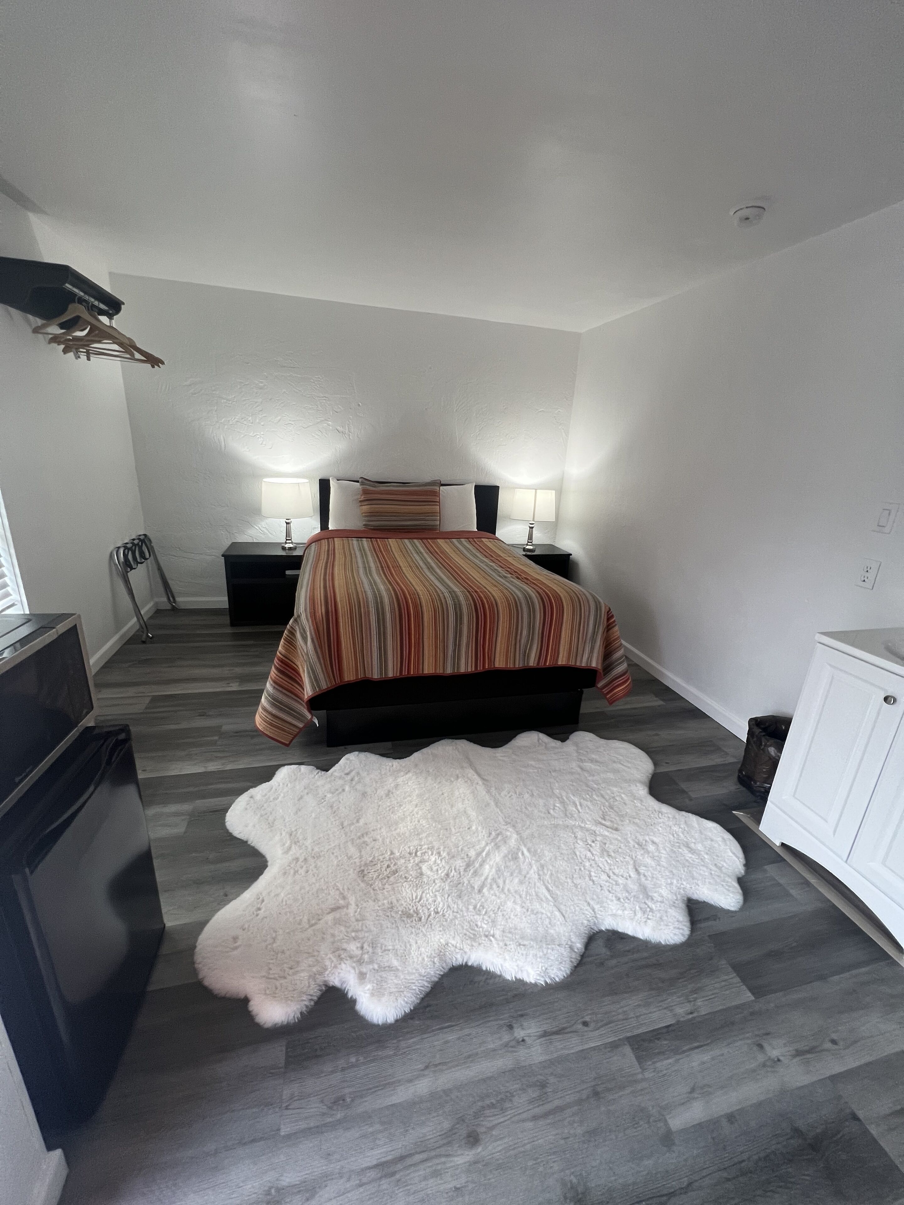 A bedroom with a bed, two bedside tables, a white rug, a TV, and a wardrobe.