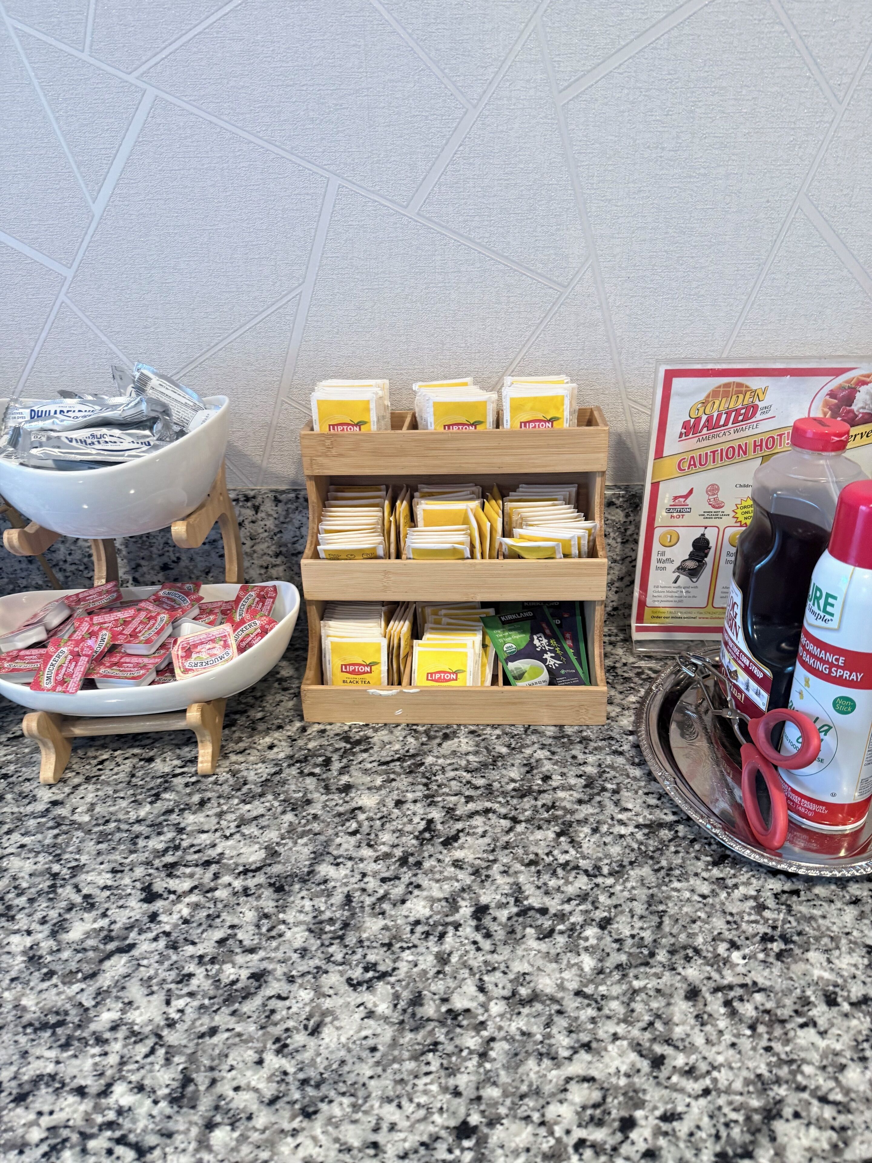 En køkkenbordplade med en træstander, der holder Lipton tepakker, en vaffeljern og en dåse bagespray.