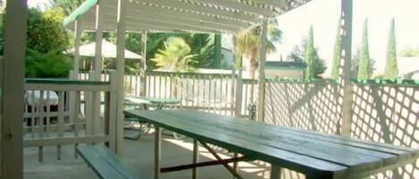 A covered outdoor area with picnic tables and a white fence.