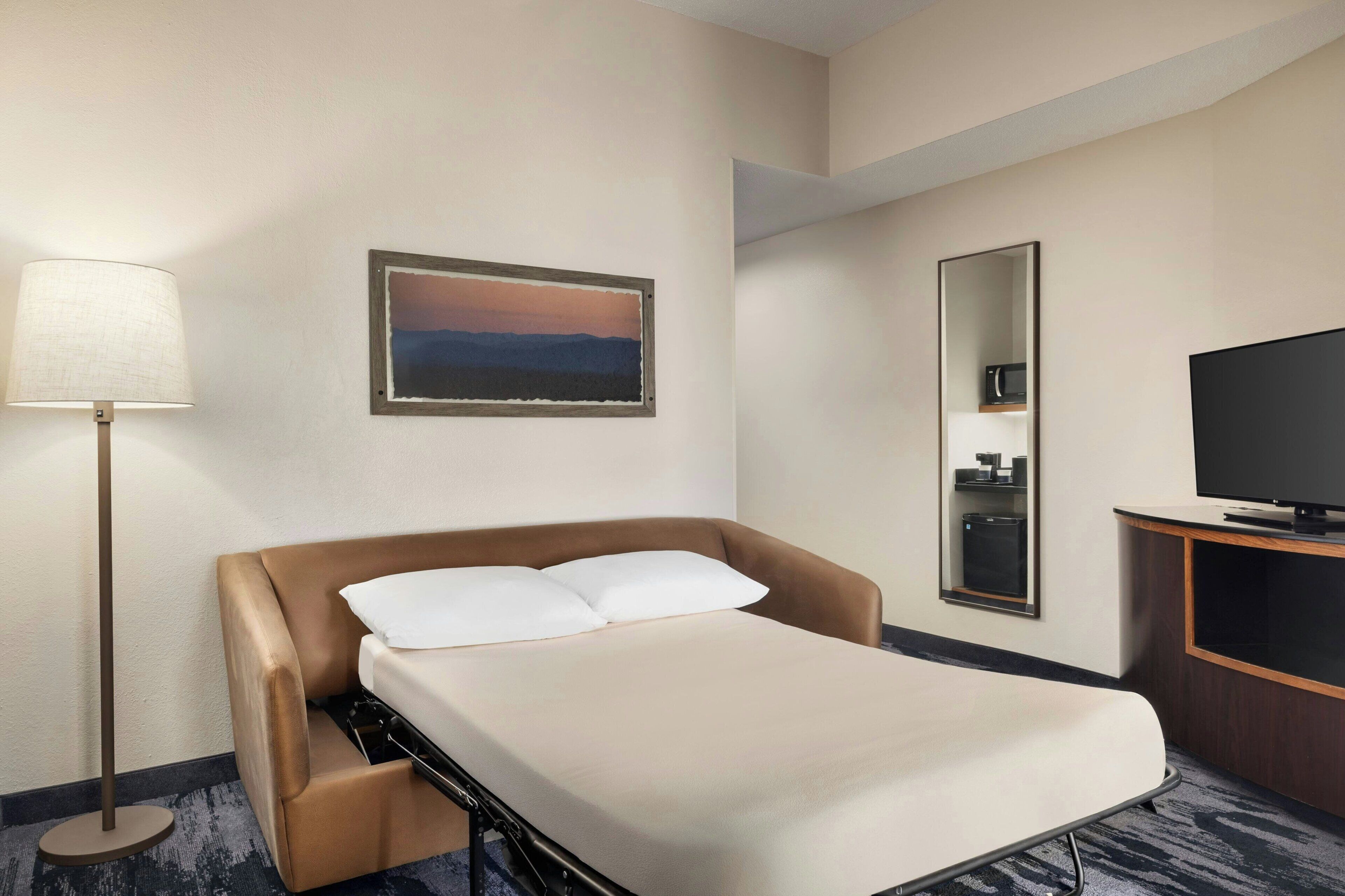 Une chambre d’hôtel avec un lit, une lampe, un tableau, un miroir et un téléviseur.
