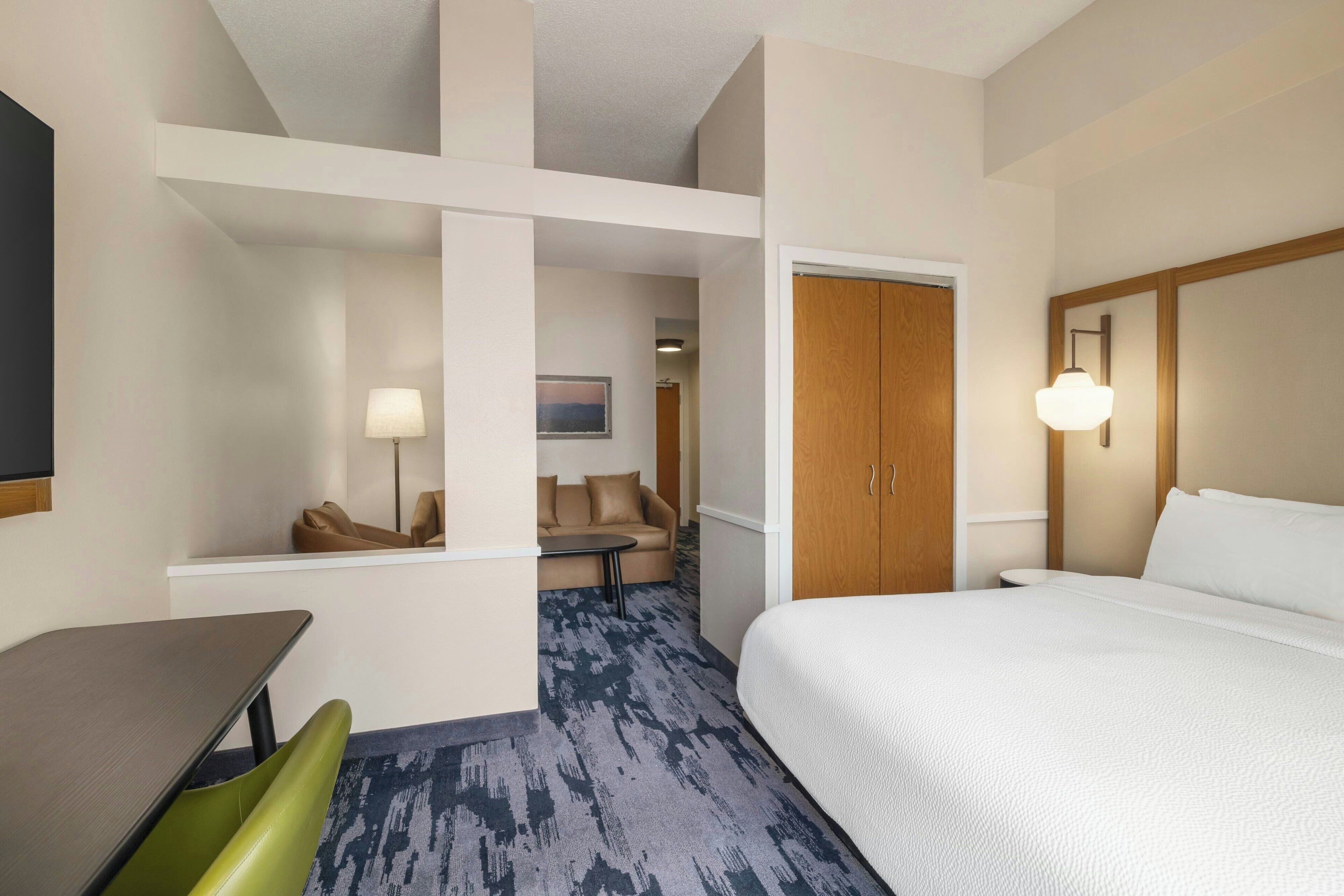 Une chambre d’hôtel comprenant un lit, un bureau, une chaise, un canapé et une porte donnant sur une autre pièce.