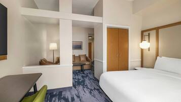 Une chambre d’hôtel comprenant un lit, un bureau, une chaise, un canapé et une porte donnant sur une autre pièce.