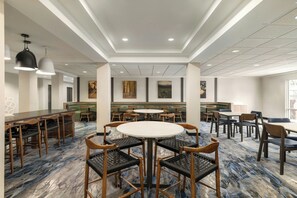 Een restaurantgedeelte van een hotel met ronde tafels, zitjes en hoge plafonds met inbouwverlichting.