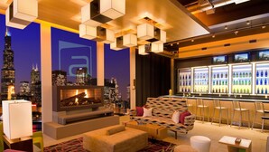 A modern lounge with a city view, a fireplace, comfortable seating, and a bar area.