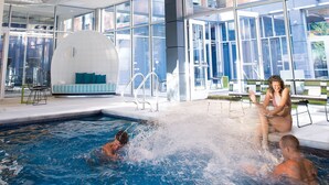 An indoor swimming pool with wooden beams, large windows, and a seating area with a view of the outside.