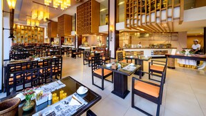 A spacious restaurant with multiple dining areas, wooden furniture, and a kitchen in the background. - Peach Blossom Resort (Karon)