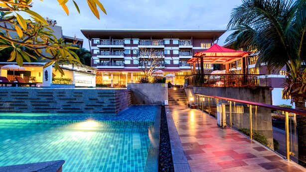 A hotel with a swimming pool, outdoor seating, and a covered area with umbrellas. - Peach Blossom Resort (Karon)