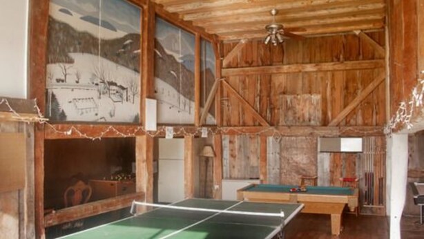A rustic room with a ping pong table, wooden walls, and a ceiling fan. - Dexter's Inn (Sunapee)