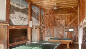 A rustic room with a ping pong table, wooden walls, and a ceiling fan. - Dexter's Inn (Sunapee)
