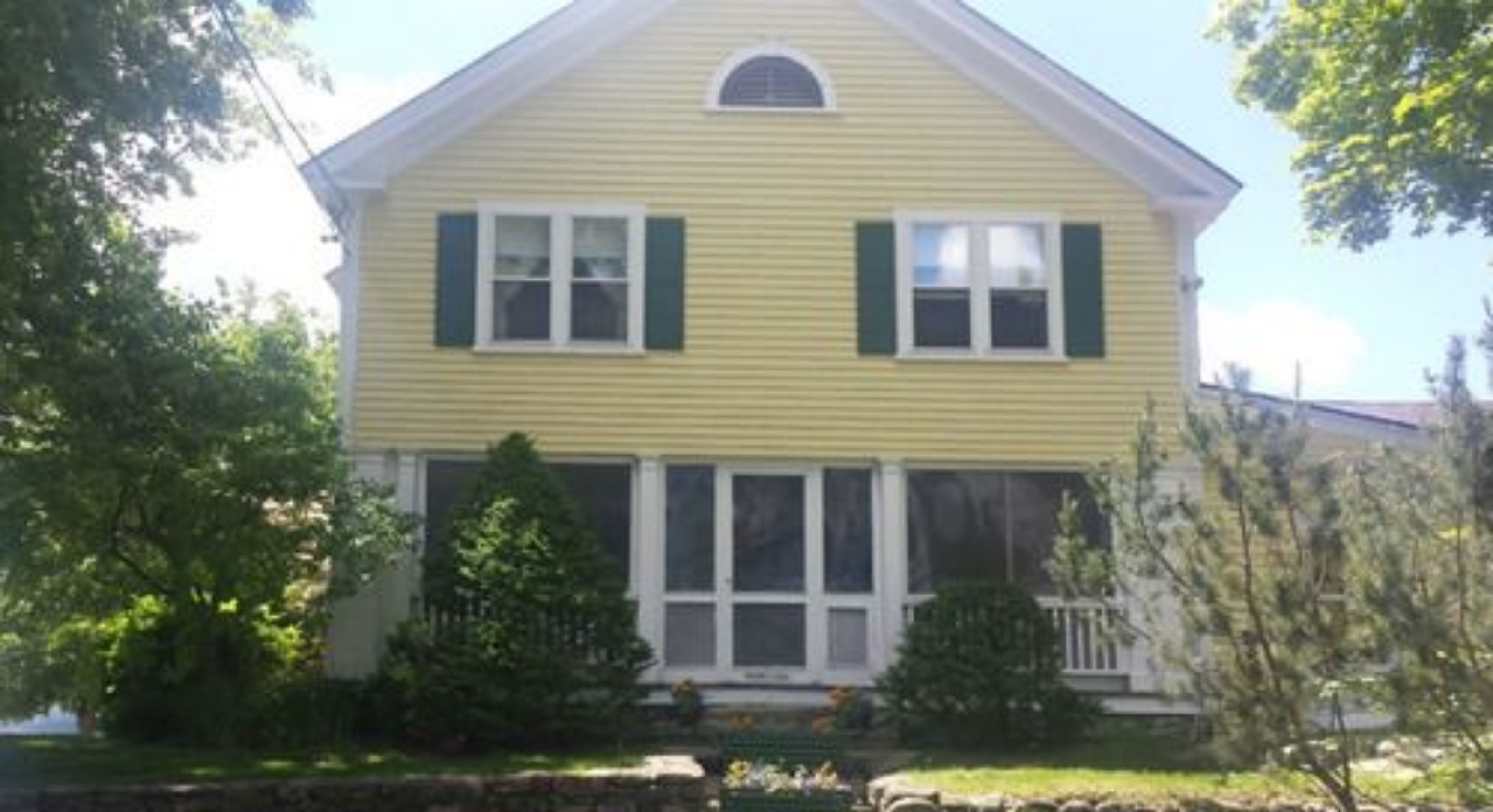 A two-story house with a gabled roof, white trim, and green shutters.