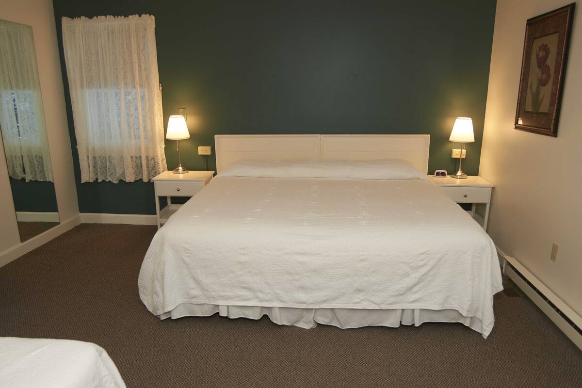 A neatly made bed with a white bedspread in a room with two bedside lamps, a mirror, and a framed picture on the wall.