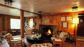 A cozy living room with a fireplace, wooden walls, and a bookshelf. - Dexter's Inn (Sunapee)