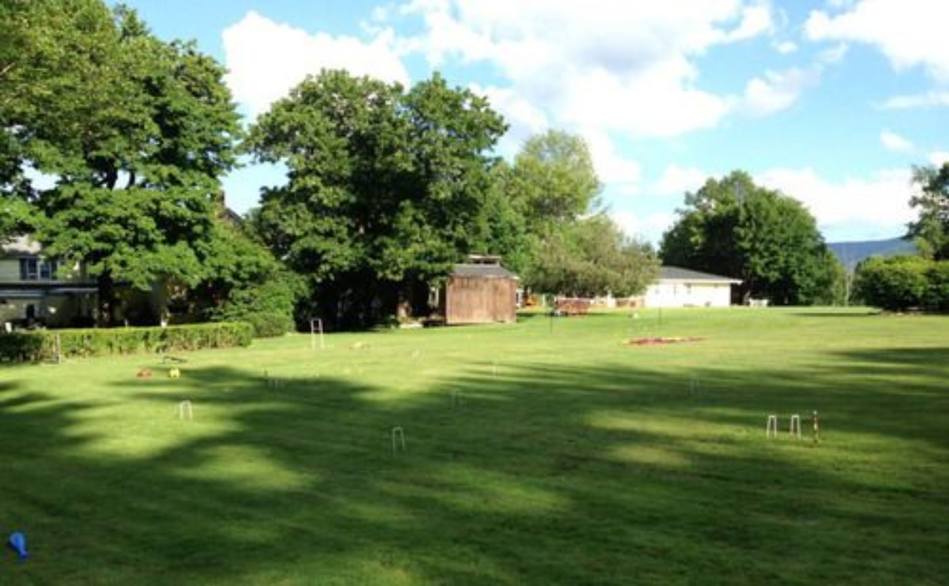 A grassy field with a small building and trees in the background.