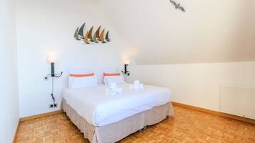 Un lit bien fait, avec du linge de lit blanc et des touches de couleur orange, un parquet en bois et des lampes fixées au mur.