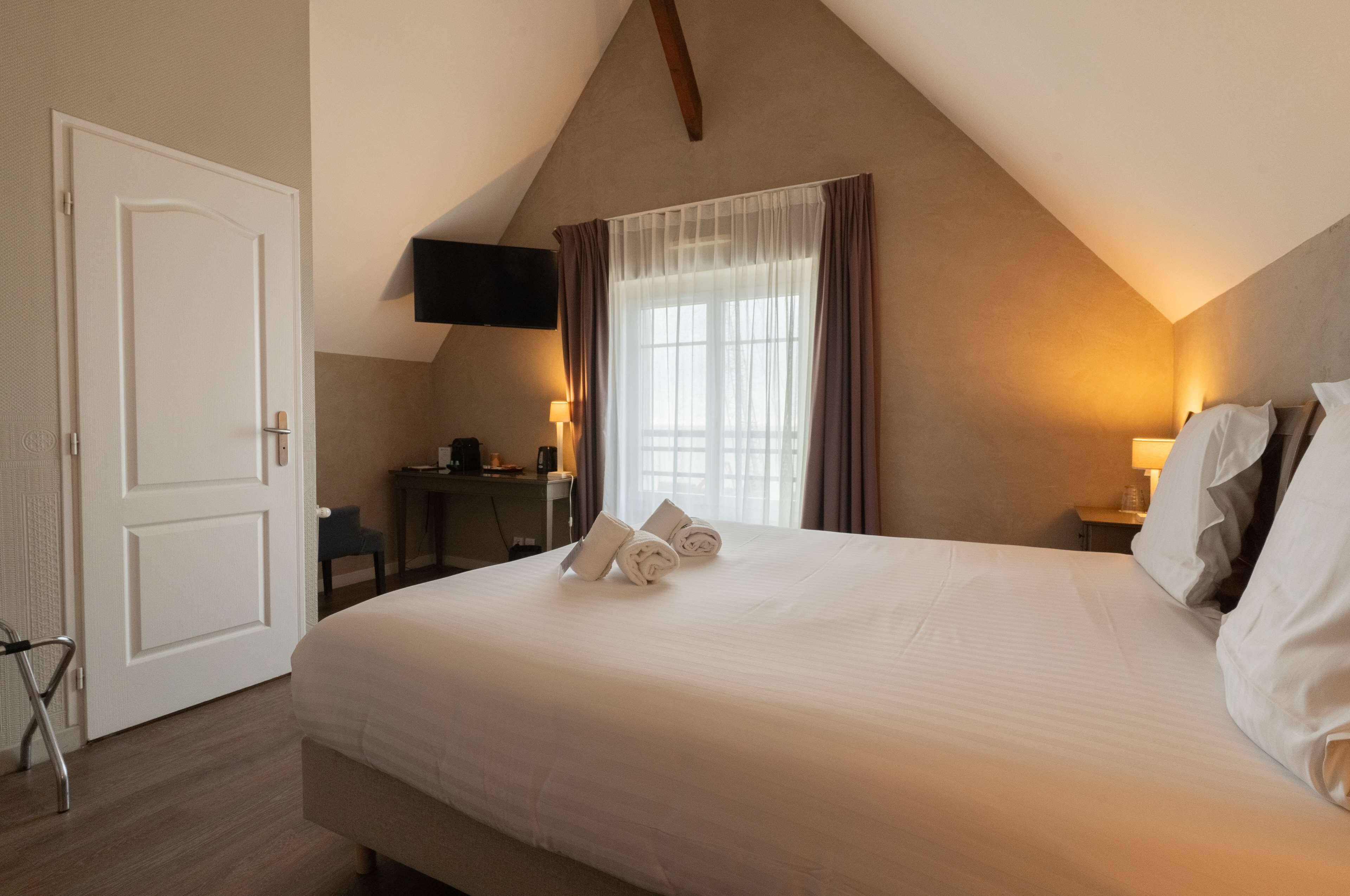 Une chambre d’hôtel avec un grand lit, un bureau, une chaise, un téléviseur fixé au mur et une fenêtre avec des rideaux.
