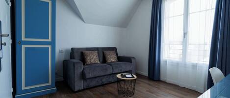 A modern living room with a dark grey sofa, a small round coffee table, and a blue cabinet.