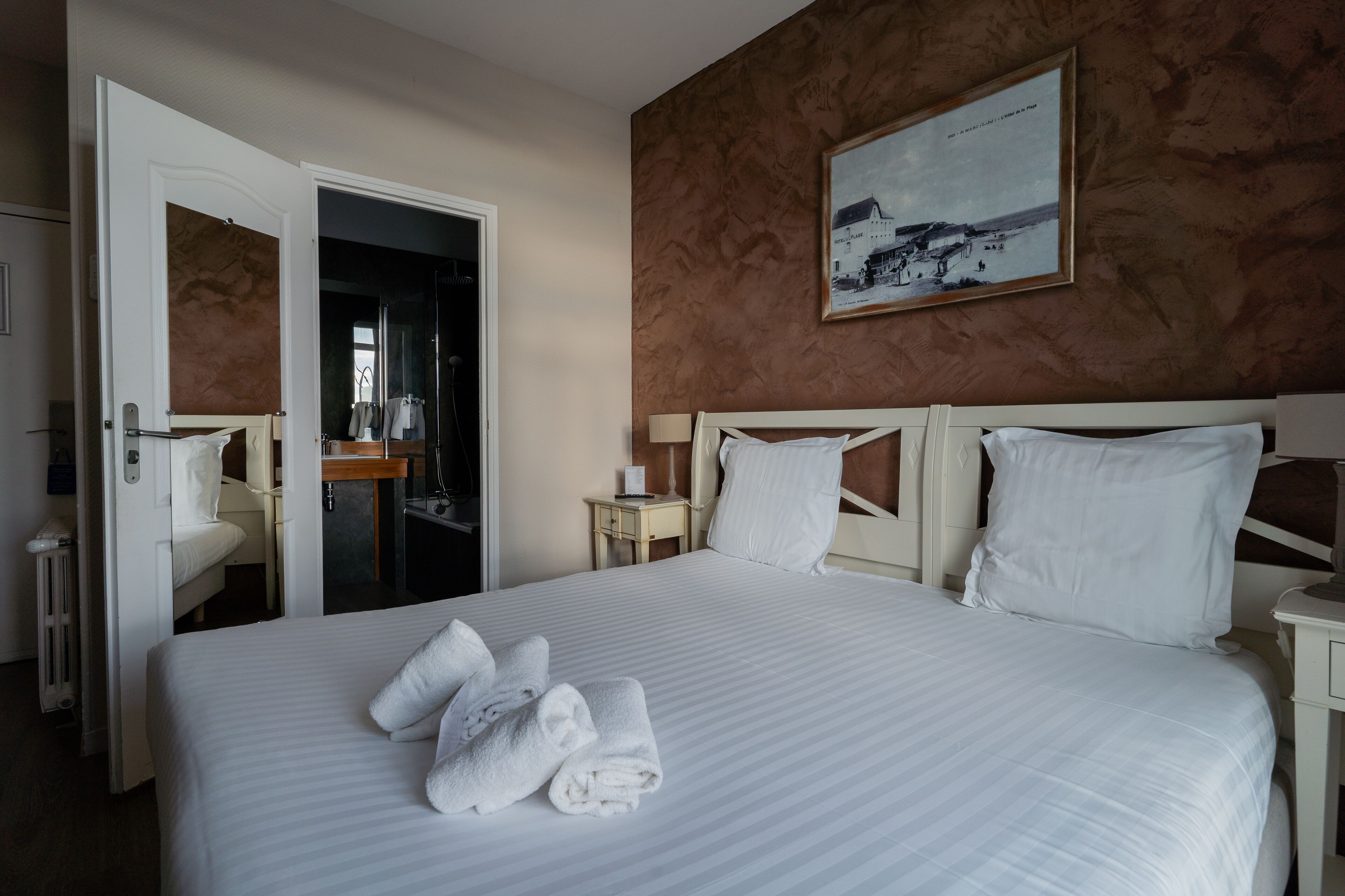 A hotel room with a large bed, a painting on the wall, and a bathroom visible through an open door.