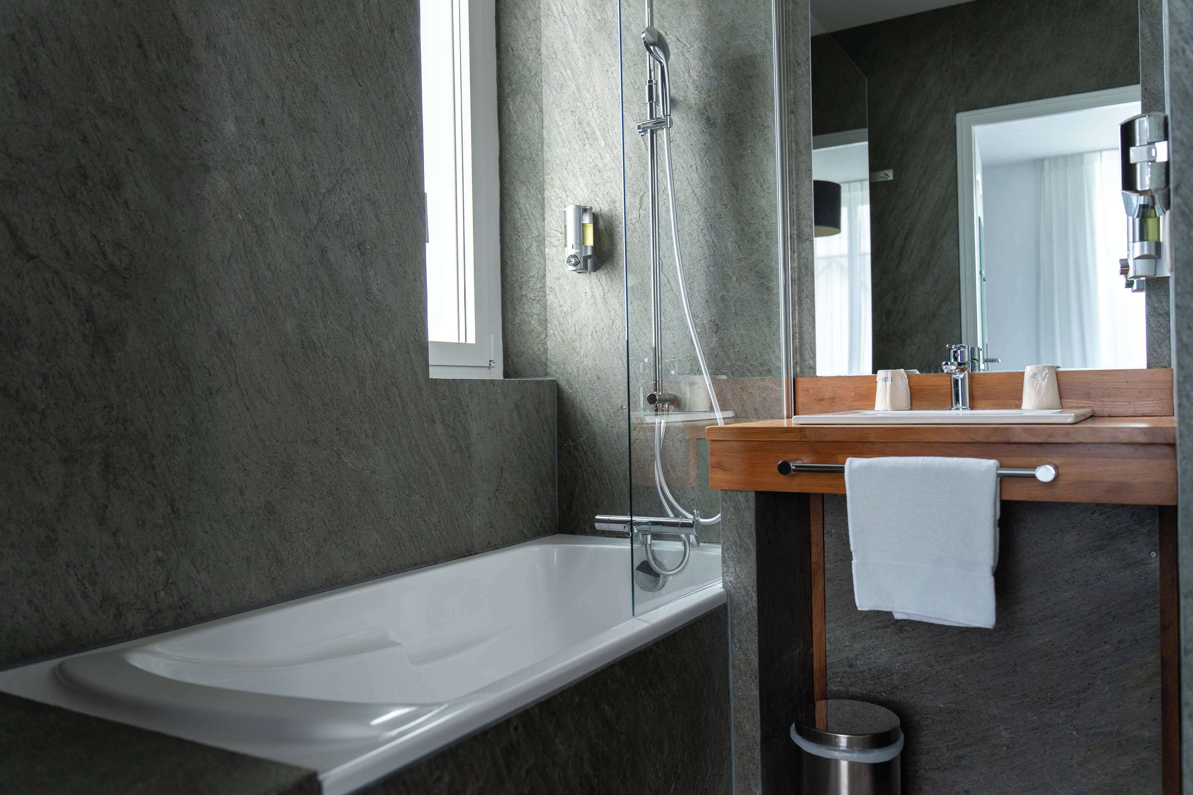 A modern bathroom with a bathtub, a wooden vanity, a mirror, and a towel rack.