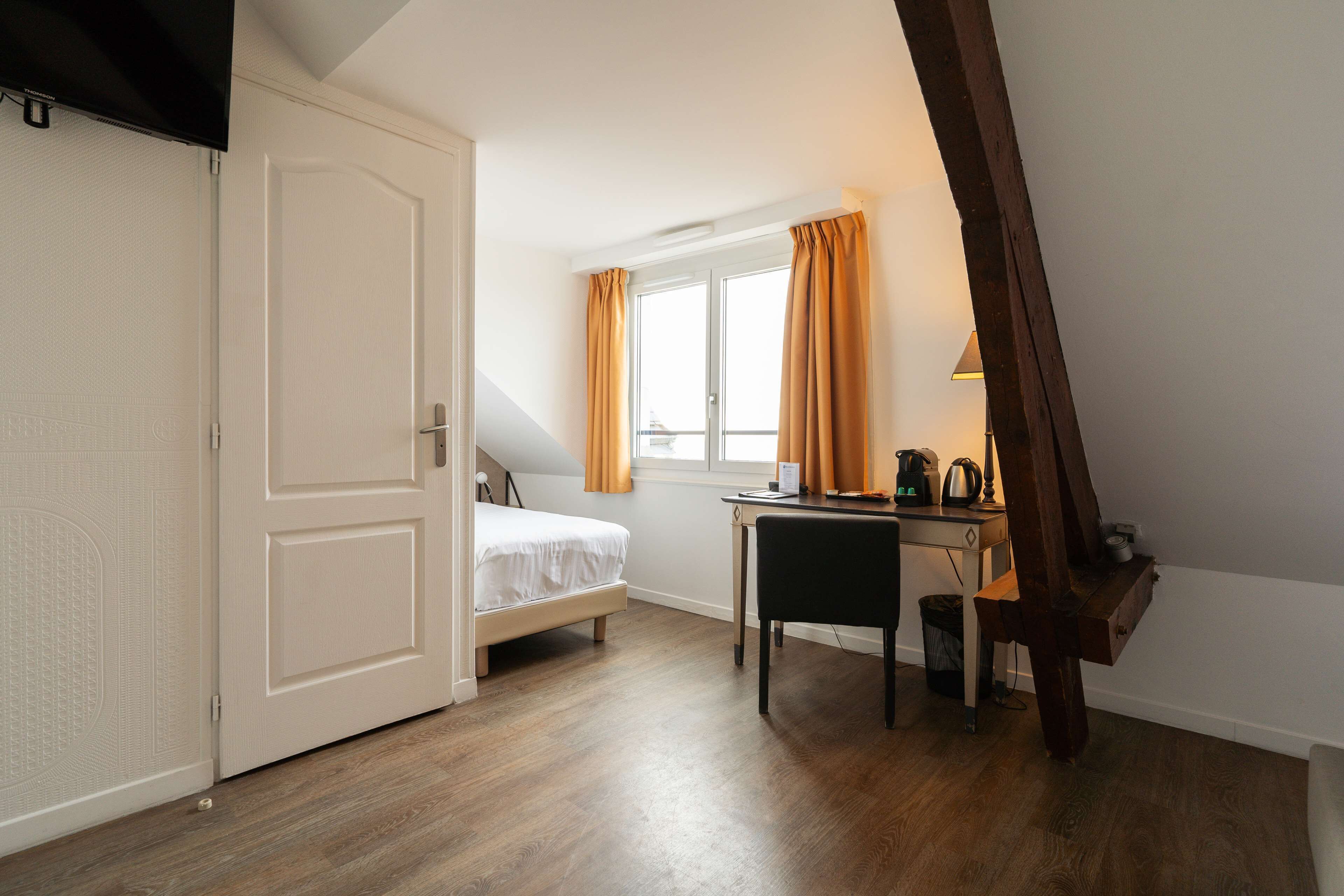 A bedroom with a bed, a desk, and a window with curtains.