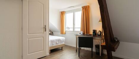 A bedroom with a bed, a desk, and a window with curtains.