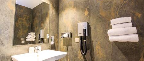 A bathroom with a white sink, a towel rack with folded towels, a hand dryer, and a mirror.