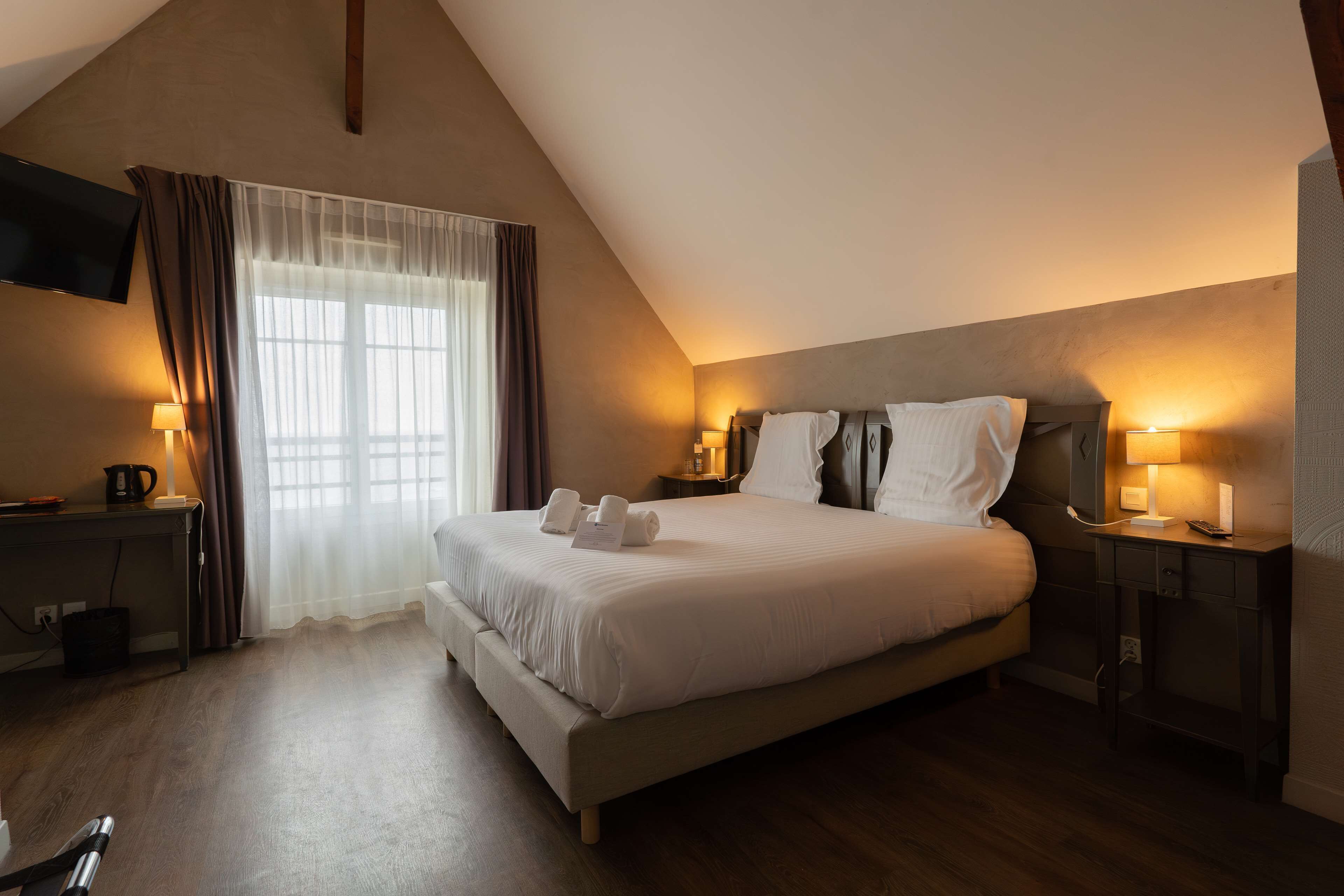 A hotel room with a large bed, bedside tables with lamps, a flat-screen TV, and a window with curtains.