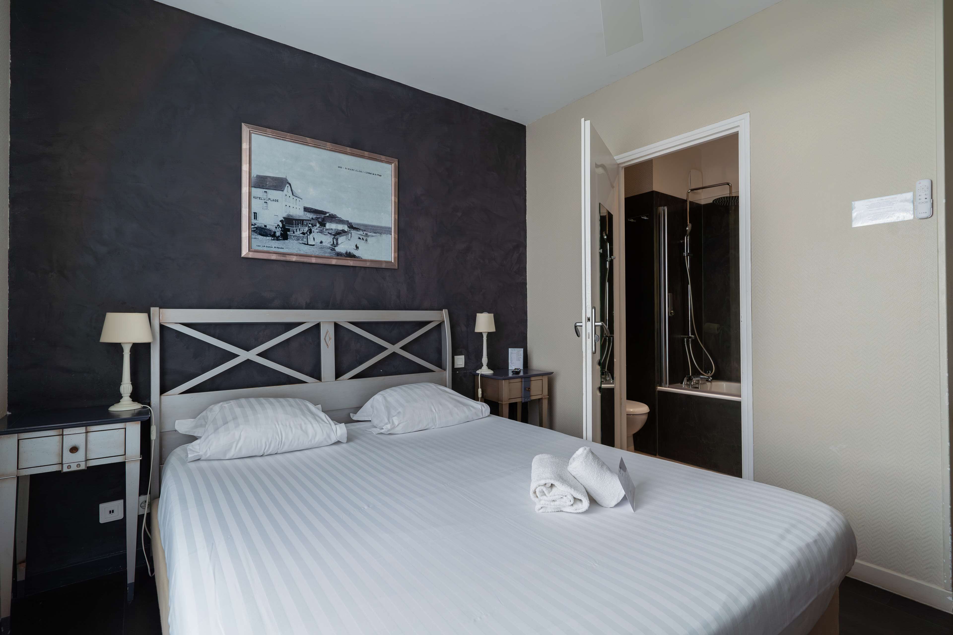 Ett hotellrum med en säng, sängbord, en inramad tavla på väggen och en badrumsdörr.