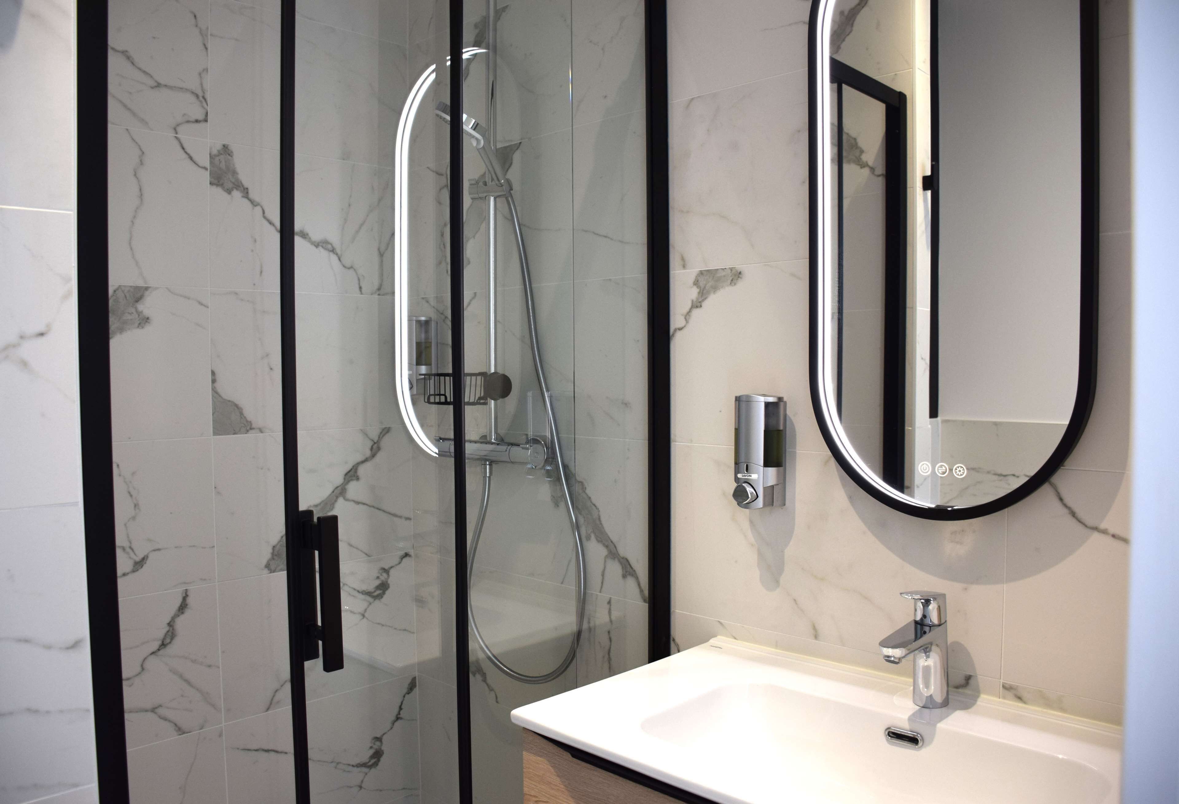 Une salle de bain moderne avec une douche à parois de verre, un lavabo blanc et un grand miroir.