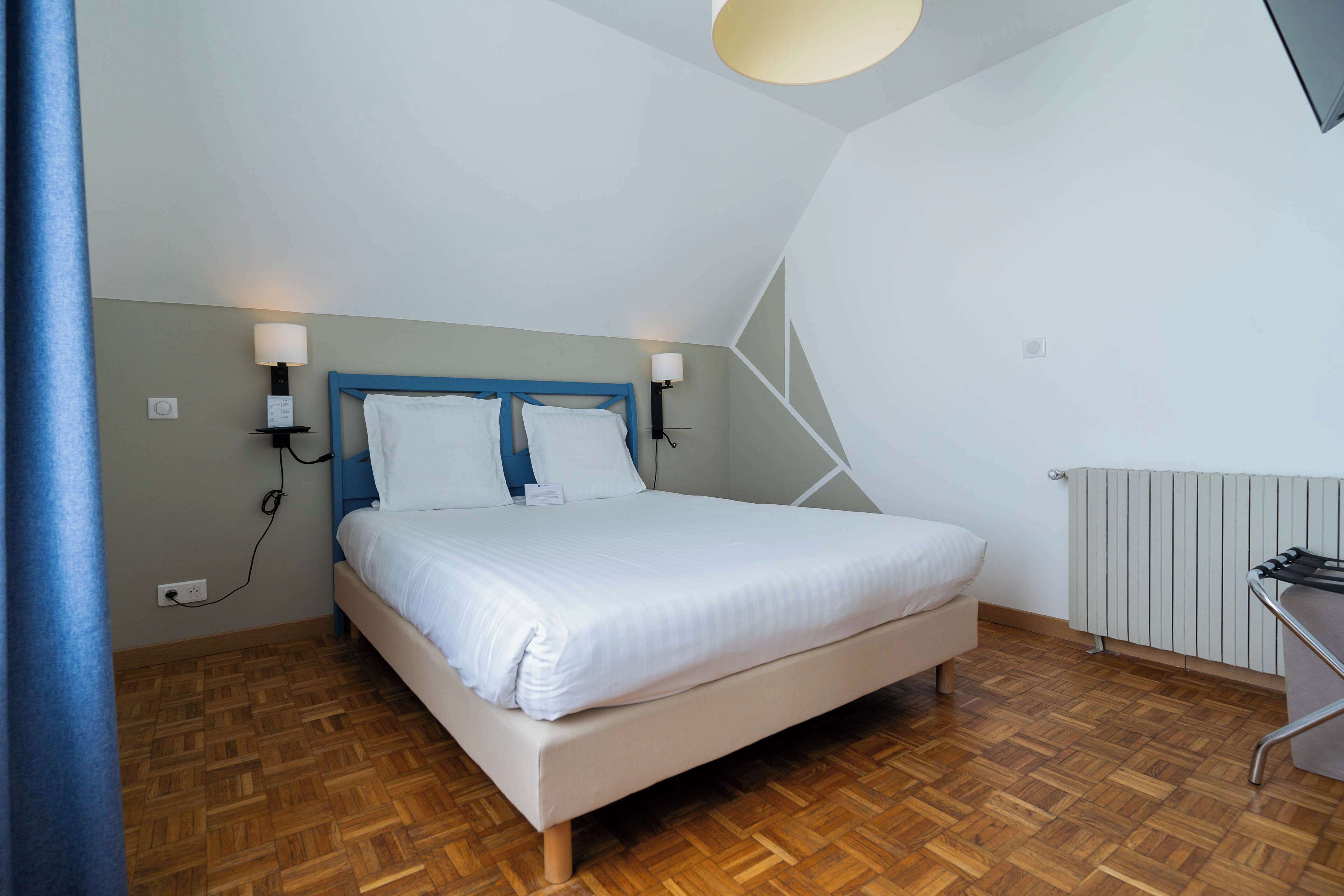 A bedroom with a bed, two wall-mounted lamps, a radiator, and a wooden floor.