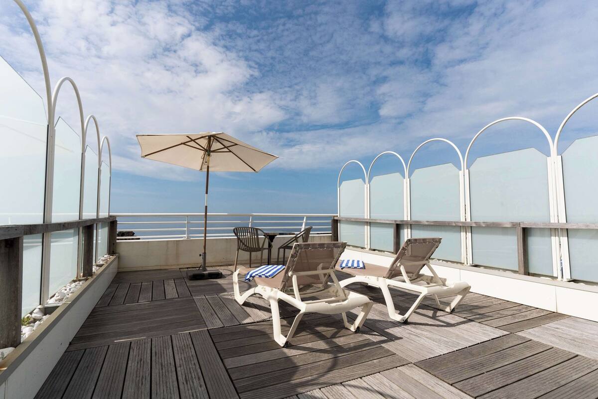 A deck with lounge chairs and an umbrella, overlooking a body of water.
