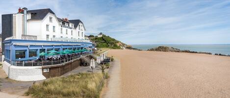 A coastal building with a terrace overlooking a sandy beach.