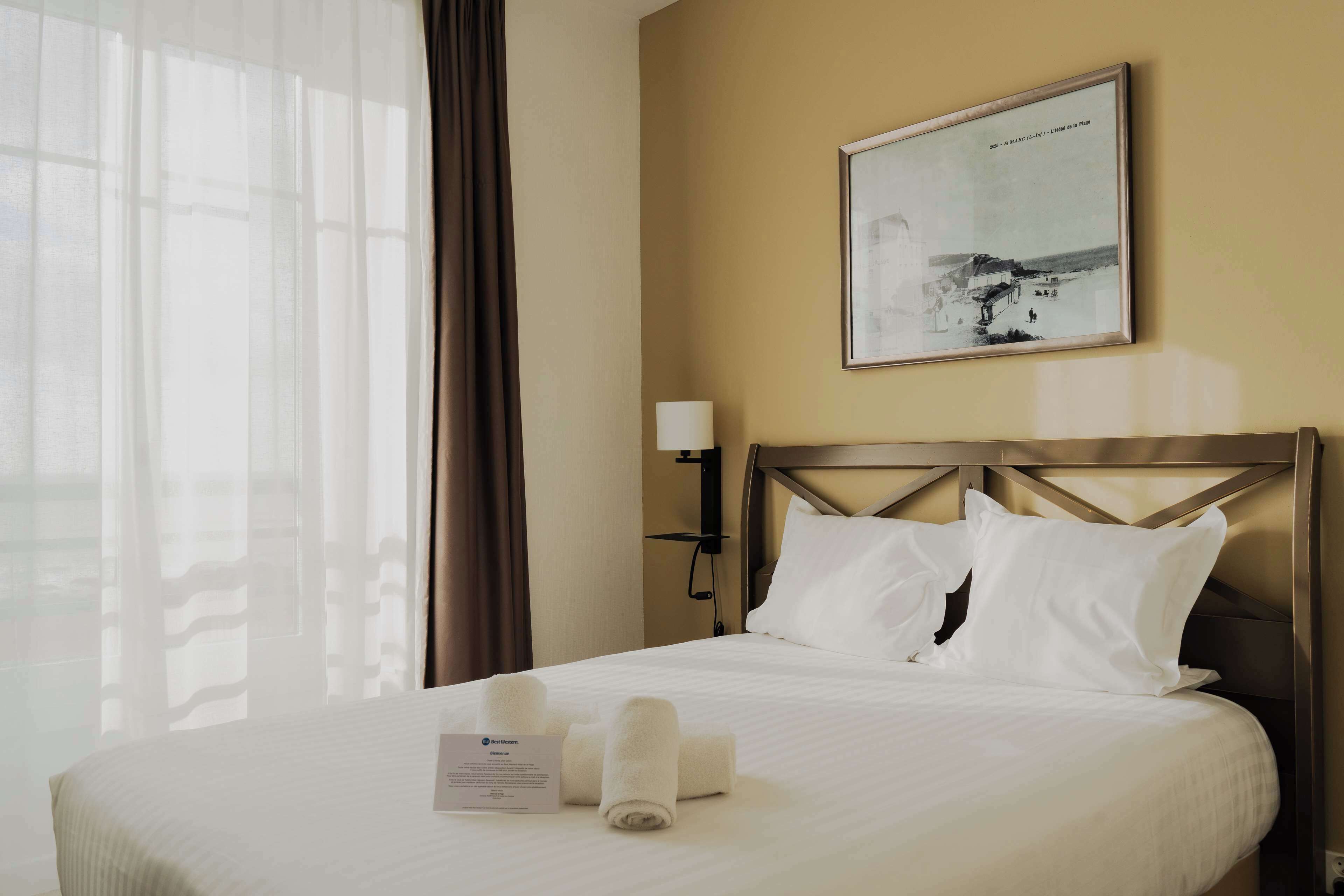 Una habitación de hotel con una cama bien hecha, un cuadro en la pared y una ventana con cortinas.